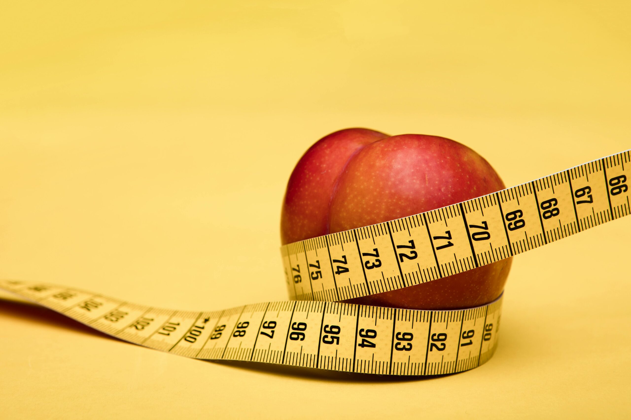 A peach wrapped with a measuring tape on a vibrant yellow background, symbolizing health and measurement.