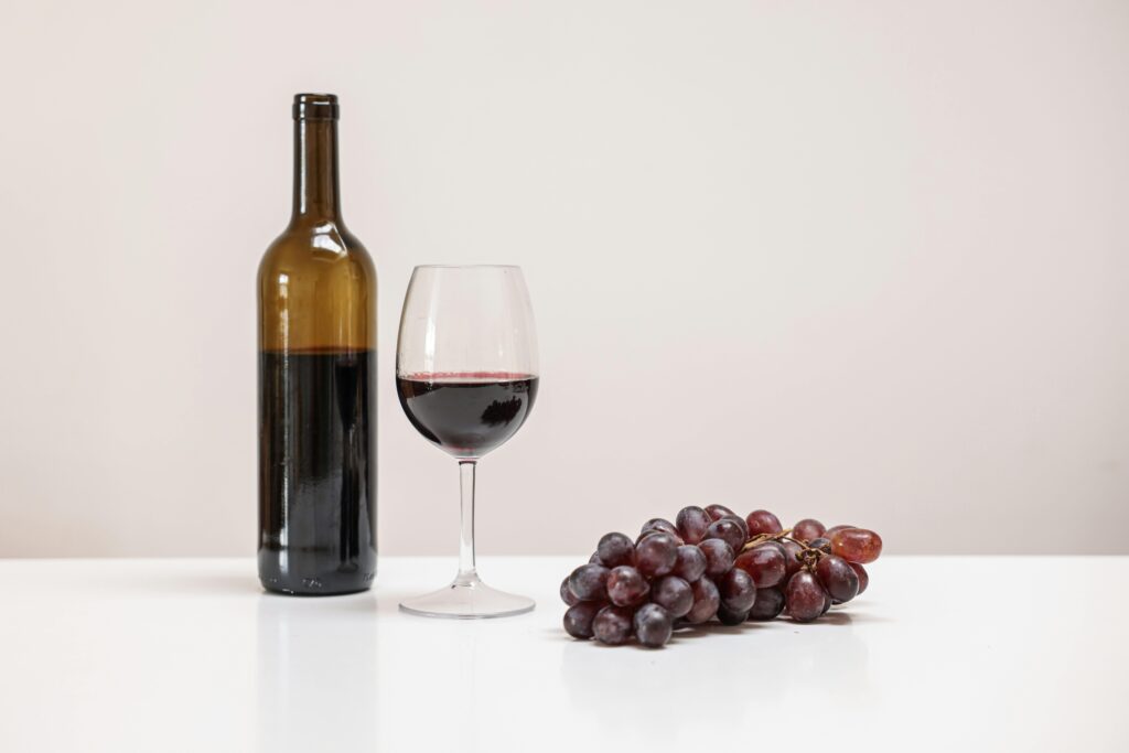 A minimalist still life featuring a wine bottle, glass, and grapes on a white table.